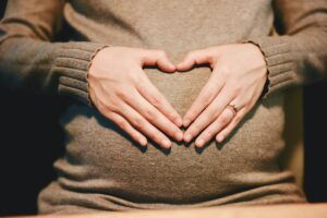 A pregnant woman is making a heart shape with her hands on her belly.