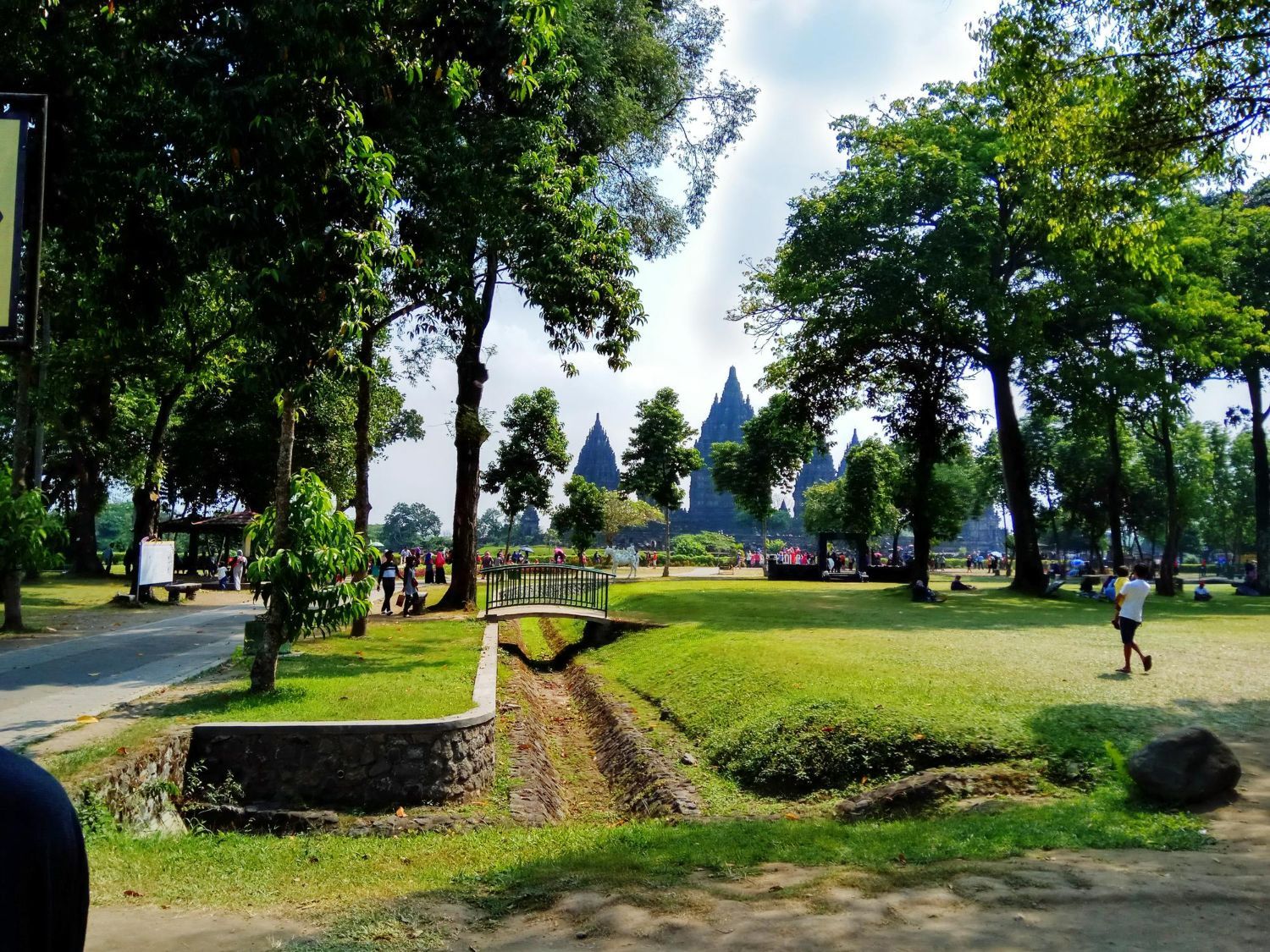 Park with green grass, trees, and distant temple structures. People present.