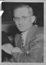 Man in glasses wearing a suit and tie, looking at the viewer.