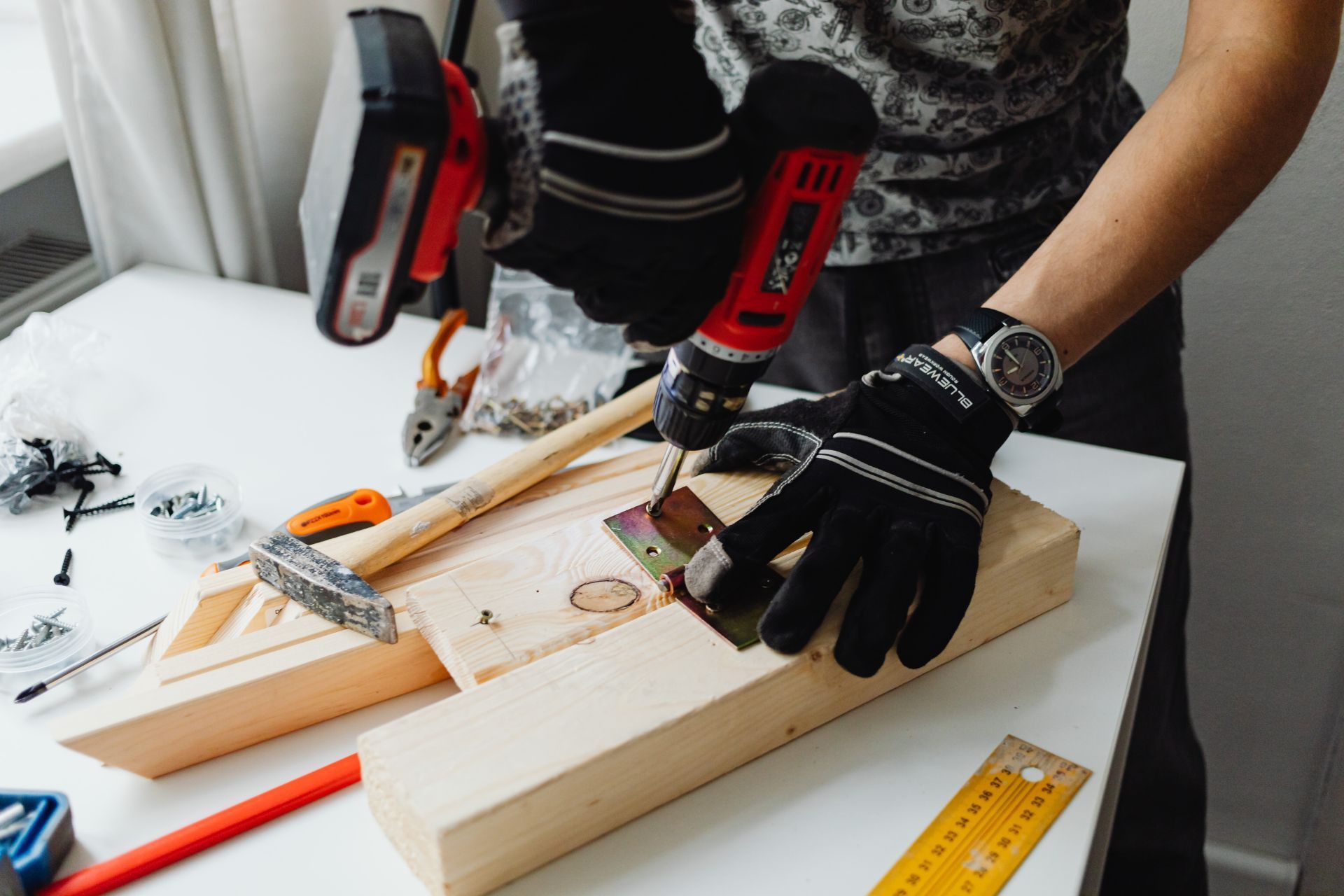 Person hammering metal bracket onto wooden plank, wearing gloves.