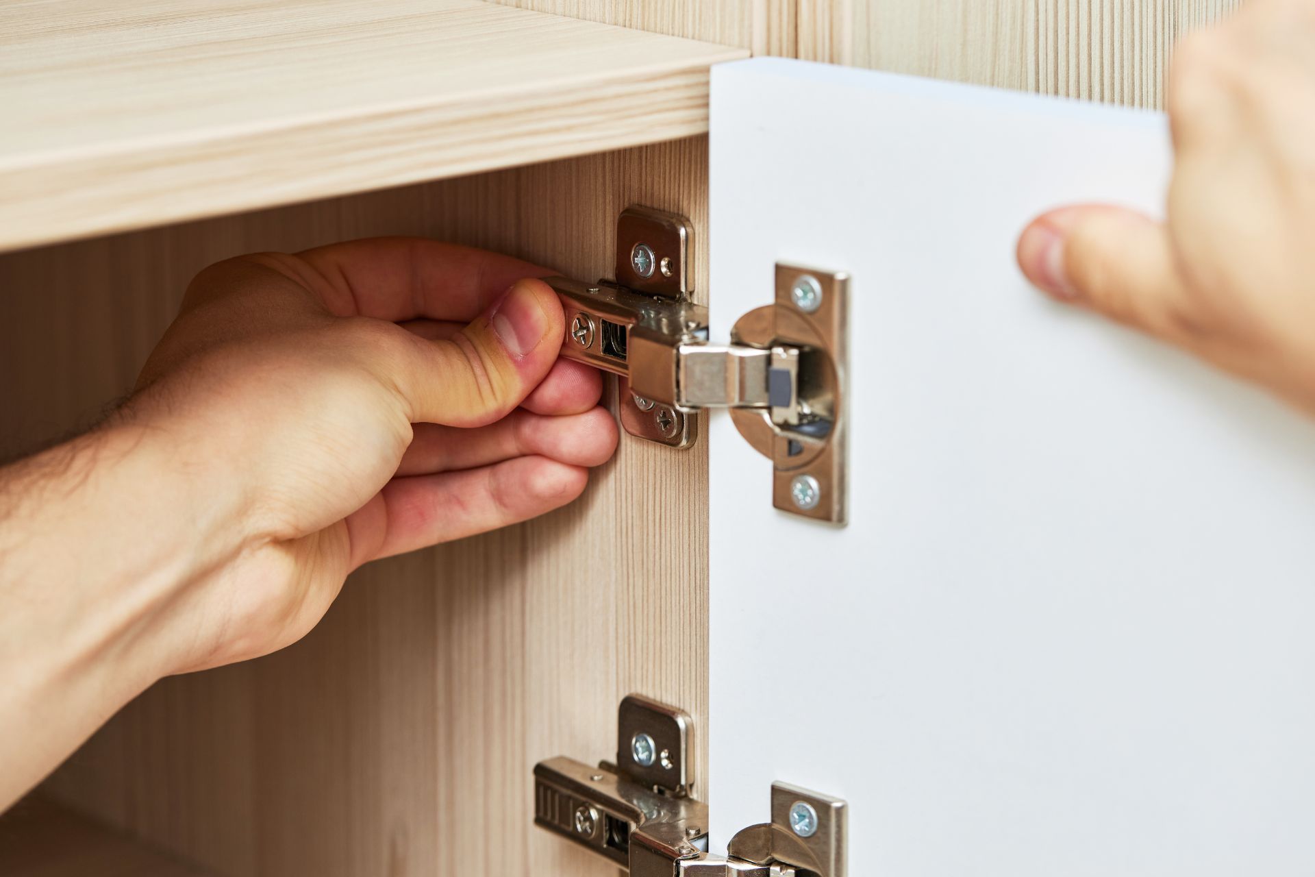 Person installing a cabinet door with hinges, white door, wooden cabinet.