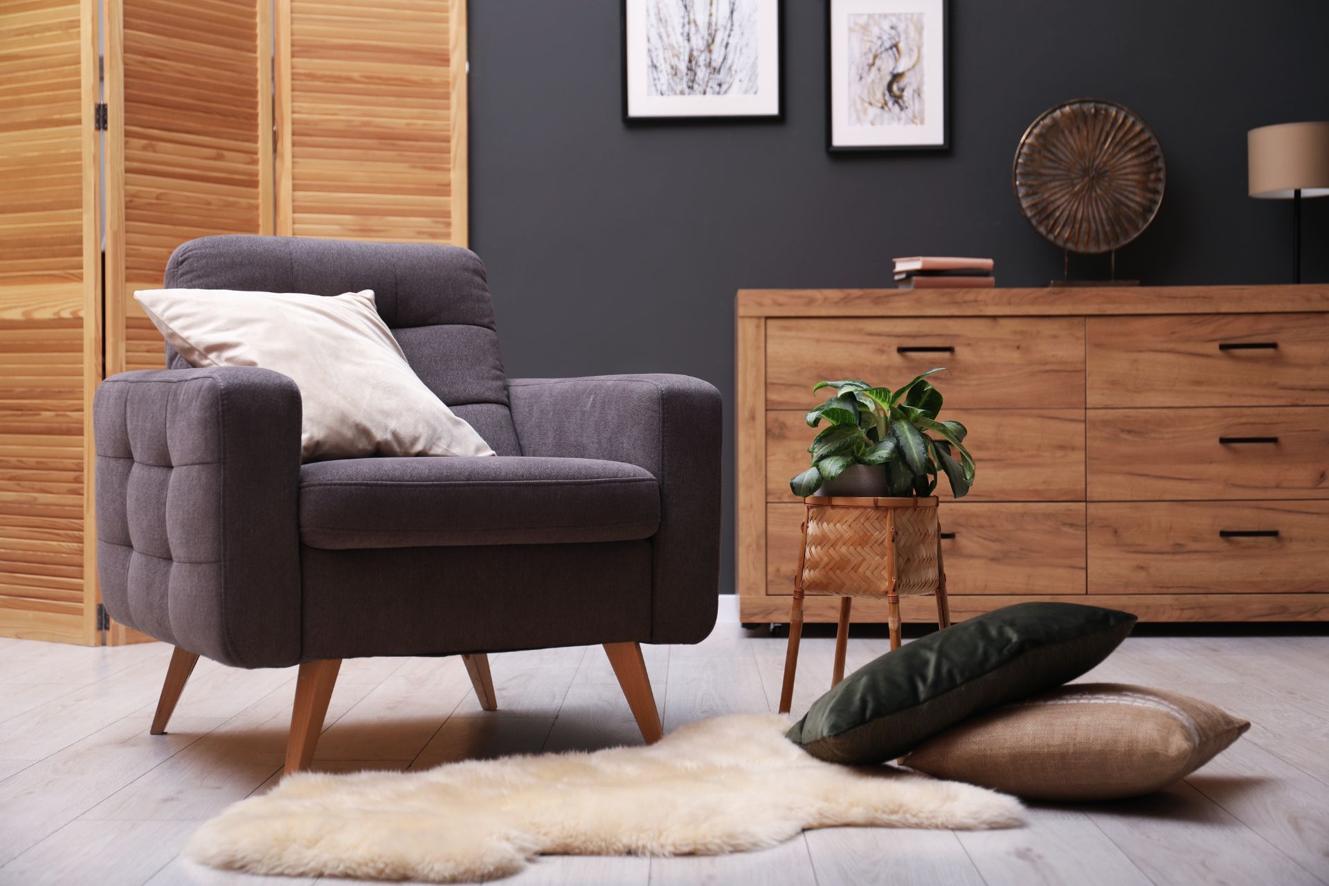 Cozy living room with gray armchair, wooden dresser, decorative pillows, and a sheepskin rug.