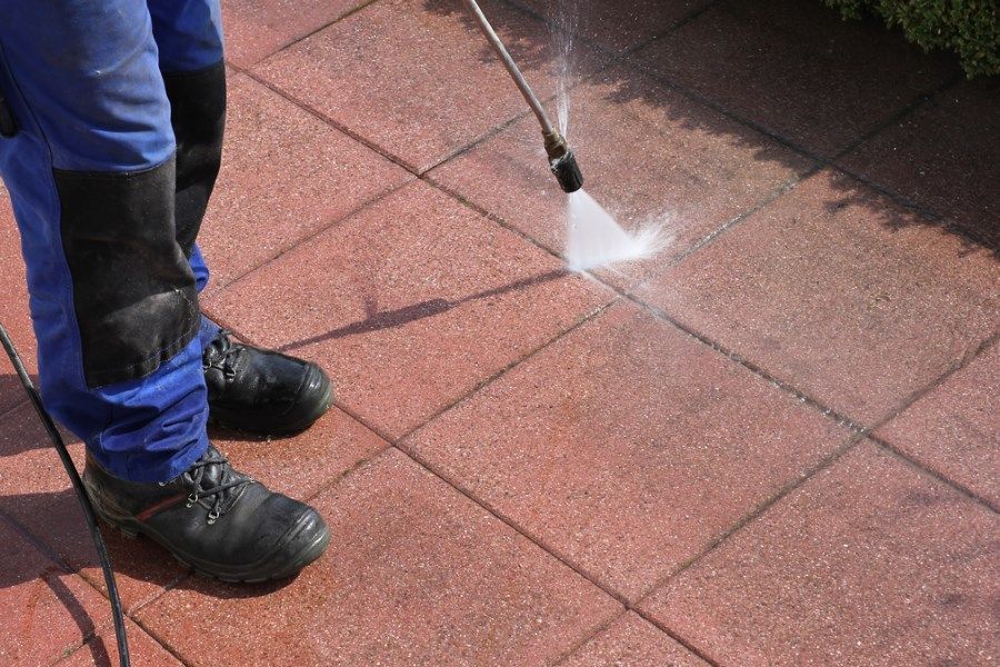 A Person Is Using A High Pressure Washer To Clean A Brick Walkway — The Guttering Cleaning Man in Tuncurry, NSW