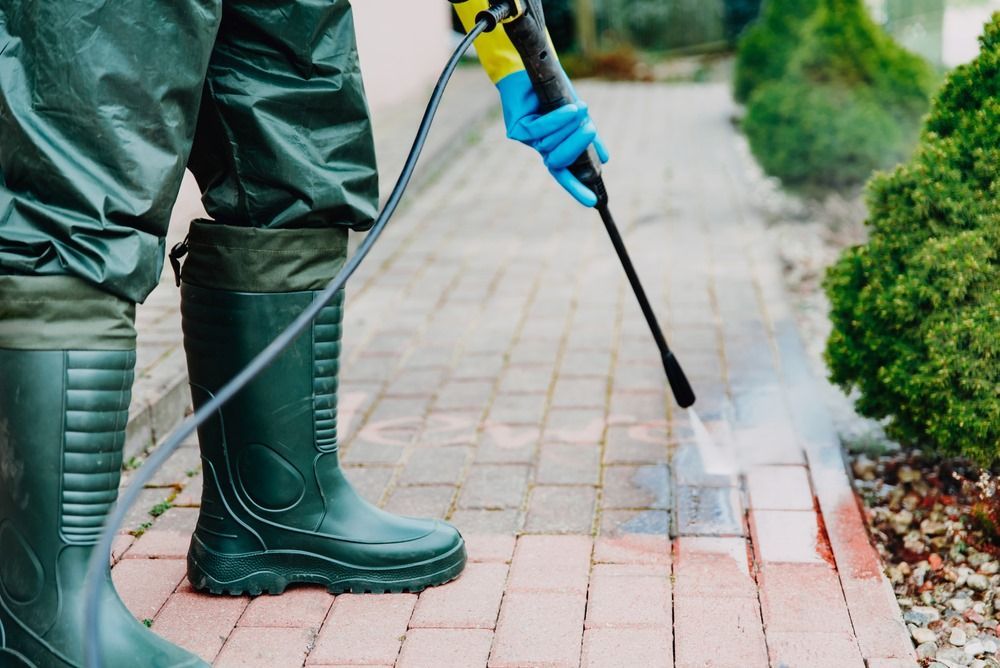 A person is spraying a brick sidewalk with a high pressure washer.