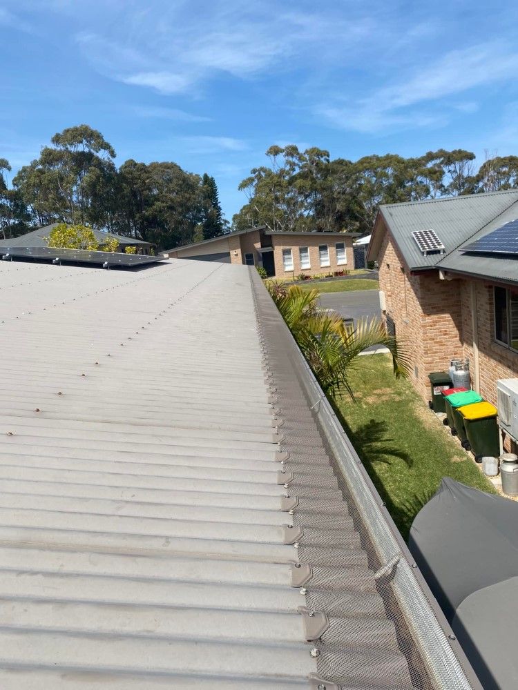 A Roof With A Gutter On It And A House In The Background — The Guttering Cleaning Man in Pacific Palms, NSW