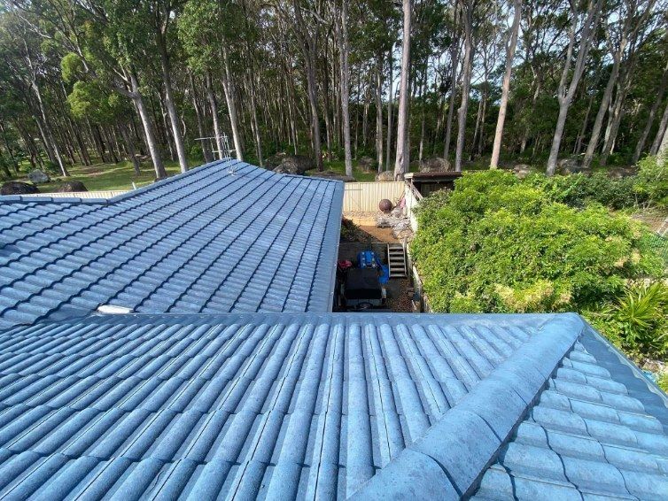 An Aerial View Of A Blue Tiled Roof With Trees In The Background — The Guttering Cleaning Man in Taree, NSW
