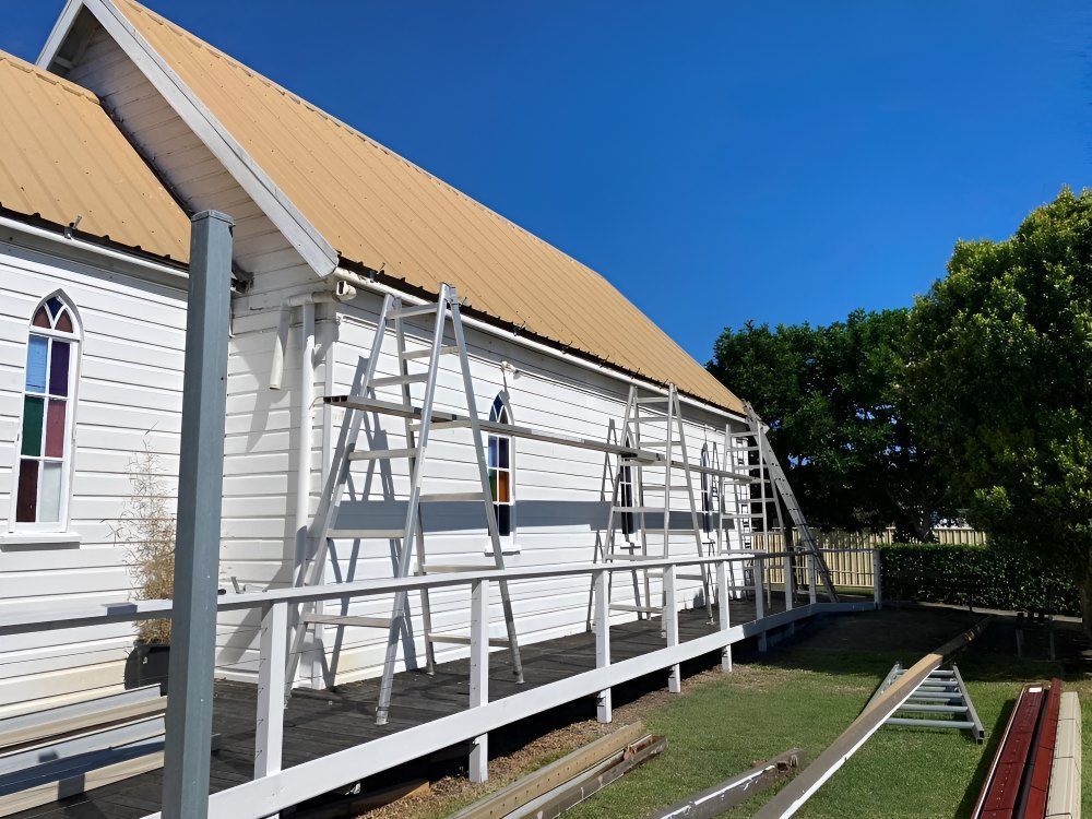 A White Building With A Yellow Roof Is Being Painted — The Guttering Cleaning Man in Forster, NSW