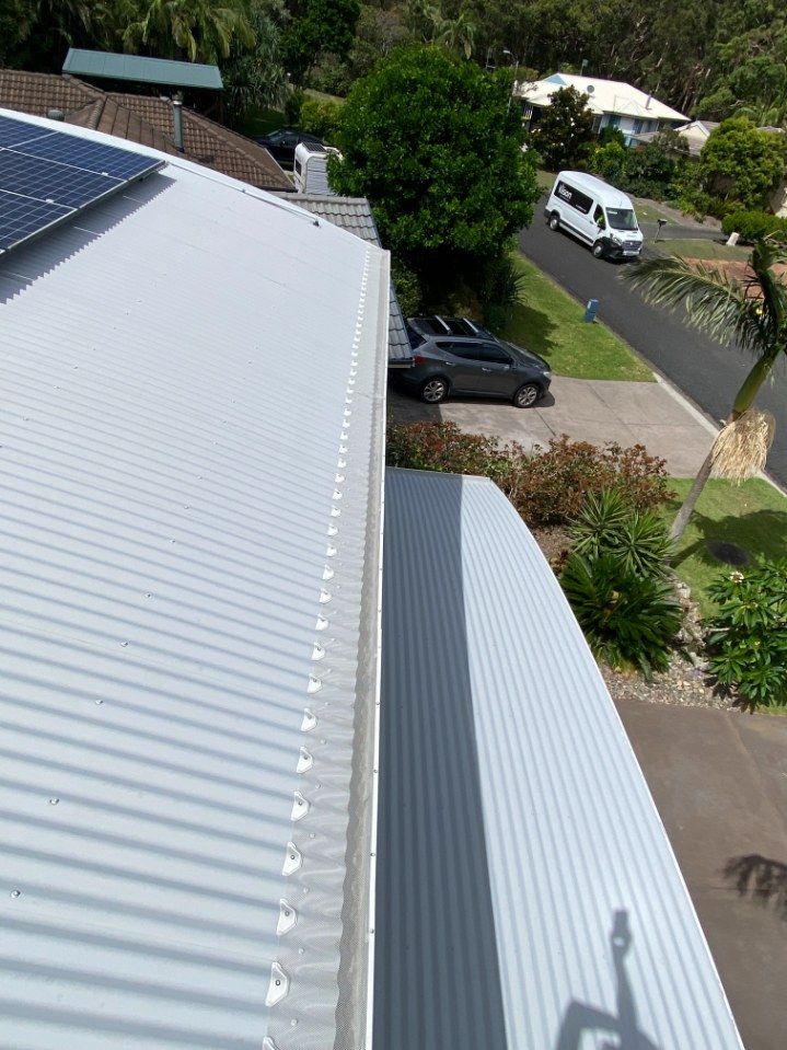 A Car Is Parked On The Side Of The Road Next To A Roof With Solar Panels On It — The Guttering Cleaning Man in Taree, NSW