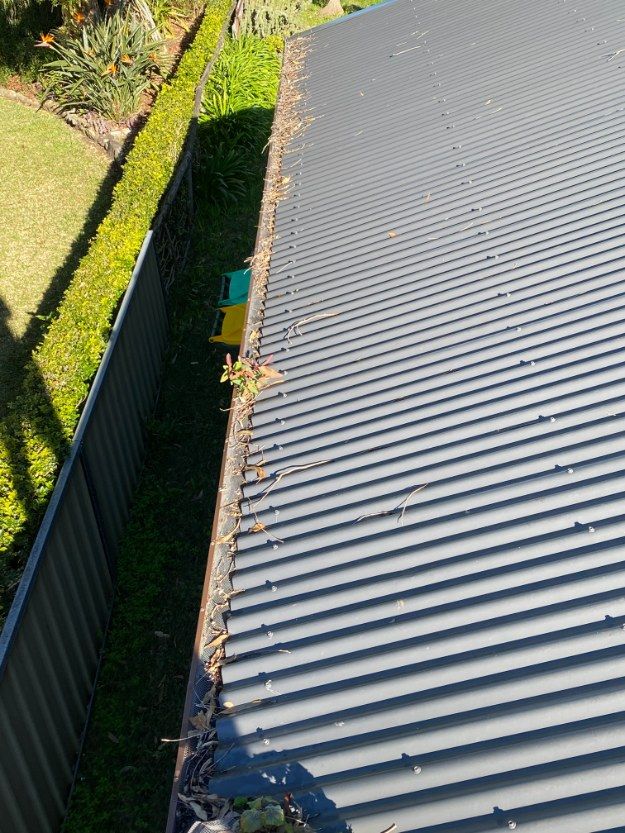 A Gutter On The Side Of A Building Next To A Fence — The Guttering Cleaning Man in Forster, NSW
