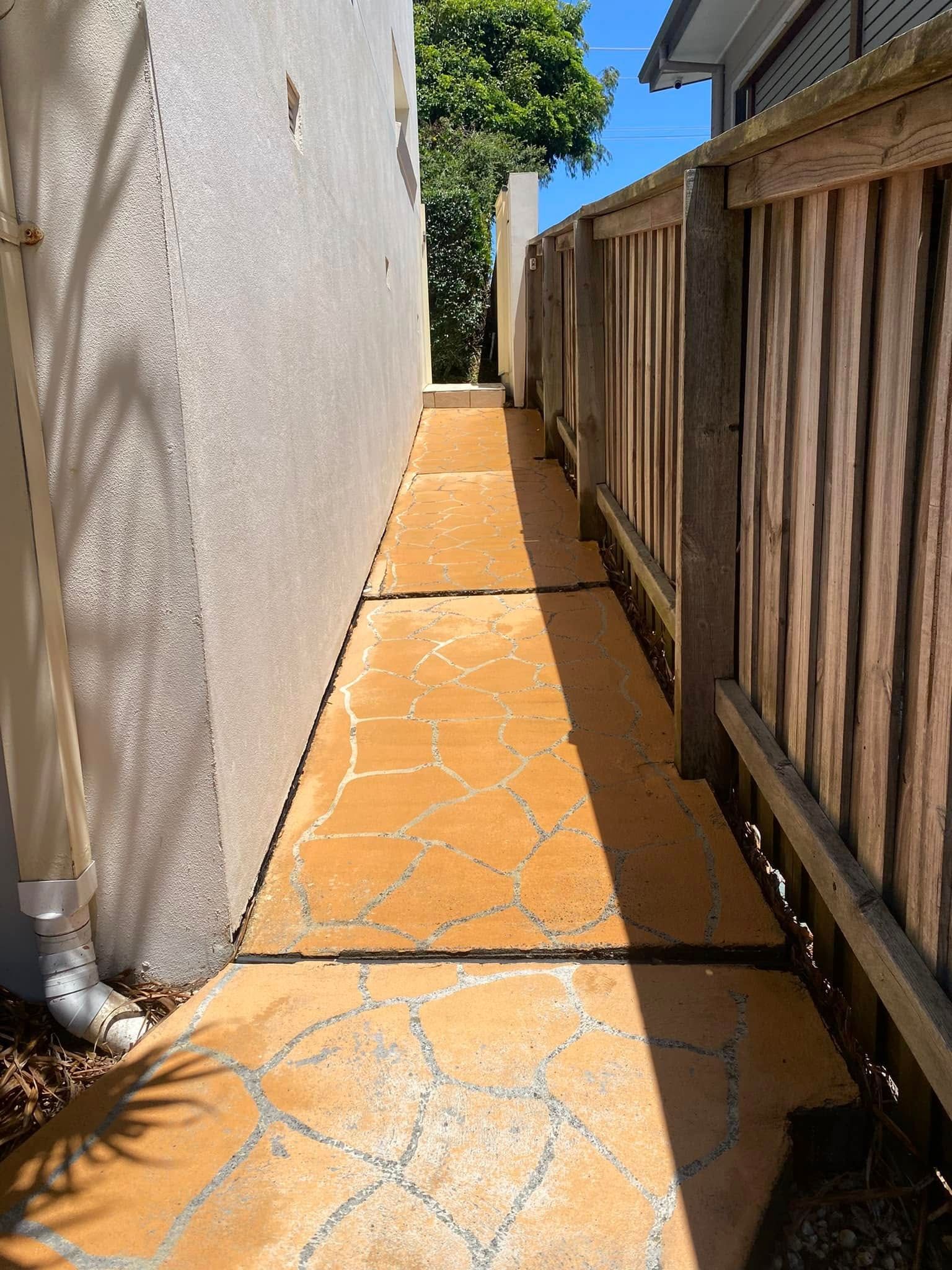 A Dirty Sidewalk Next To A House With A Wooden Fence — The Guttering Cleaning Man in Forster, NSW
