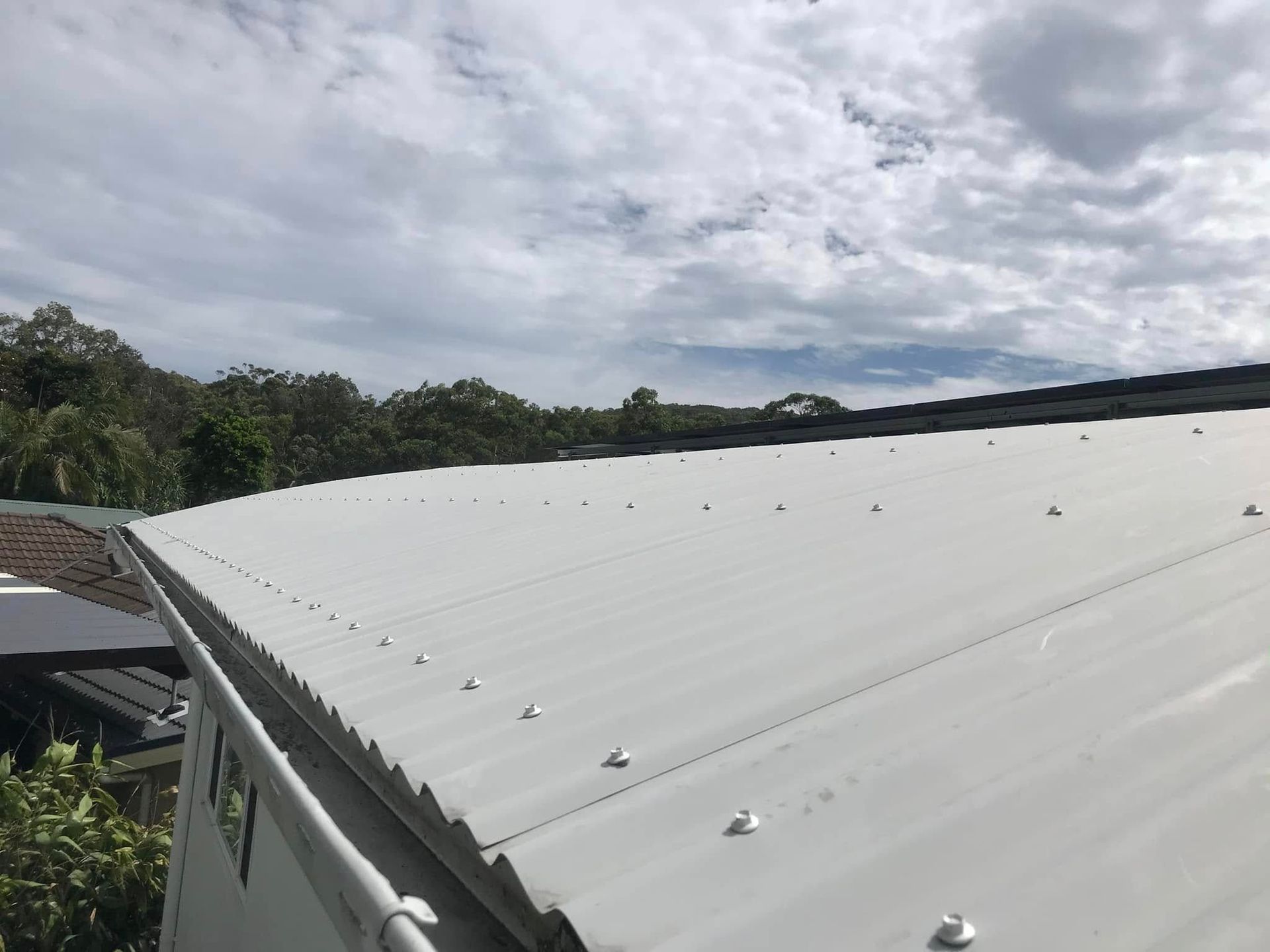 A Gutter On The Roof Of A House Next To A Fence — The Guttering Cleaning Man in Forster, NSW