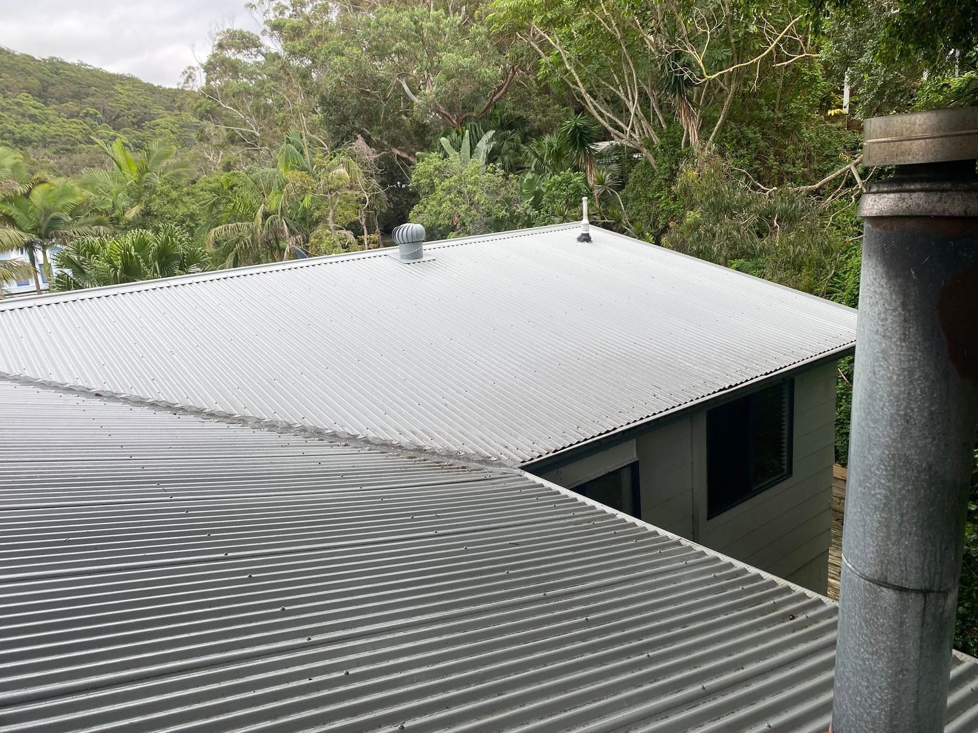 A Person Is Using A High Pressure Washer To Clean A Wooden Fence — The Guttering Cleaning Man in Taree, NSW