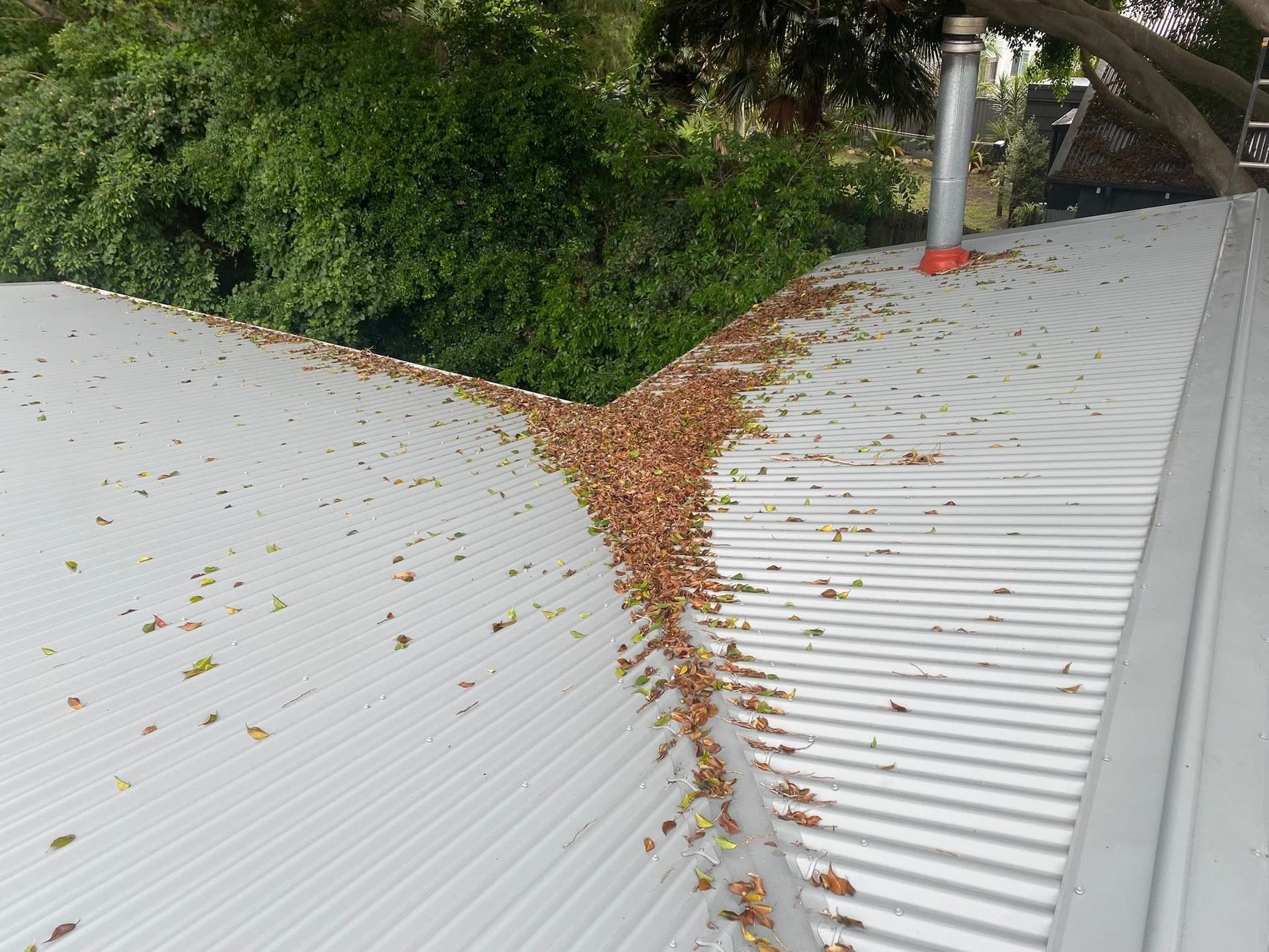 A Person Is Cleaning A Gutter With A Brush And Leaves — The Guttering Cleaning Man in Forster, NSW