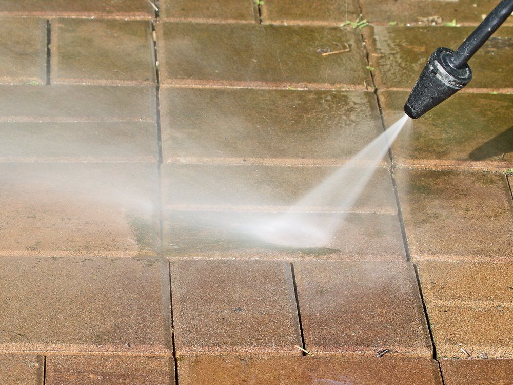 A Person Is Using A High Pressure Washer To Clean A Brick Walkway — The Guttering Cleaning Man in Taree, NSW