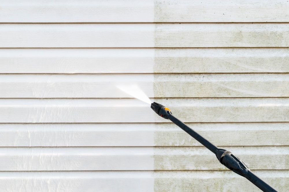 A Person Is Cleaning The Side Of A House With A High Pressure Washer — The Guttering Cleaning Man in Old Bar, NSW