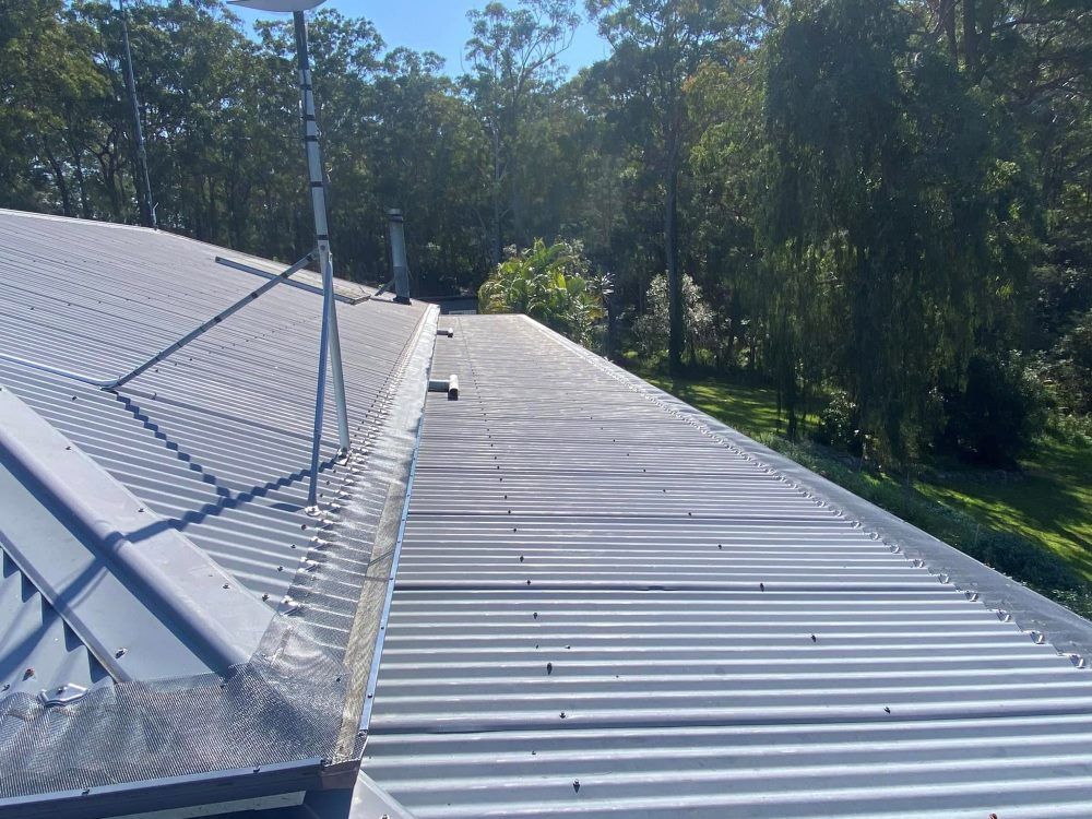 A roof with a gutter on it and trees in the background.