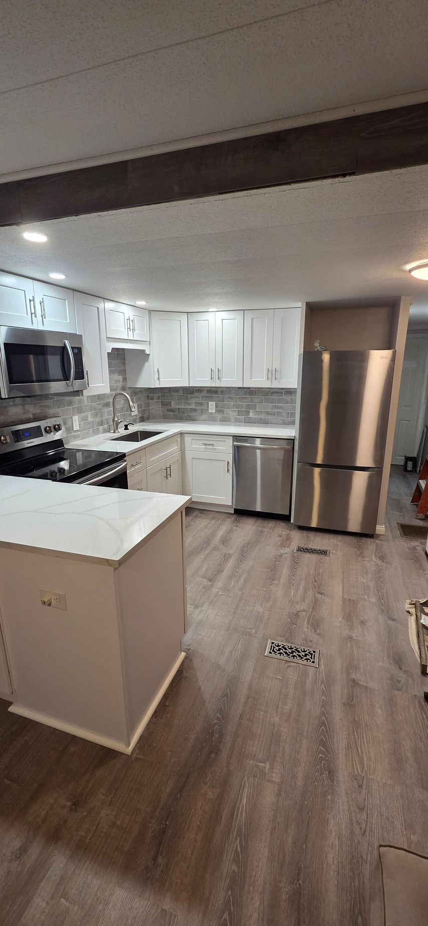 Empty modern kitchen with white cabinets, stainless steel refrigerator, gray countertops, and wood-look flooring