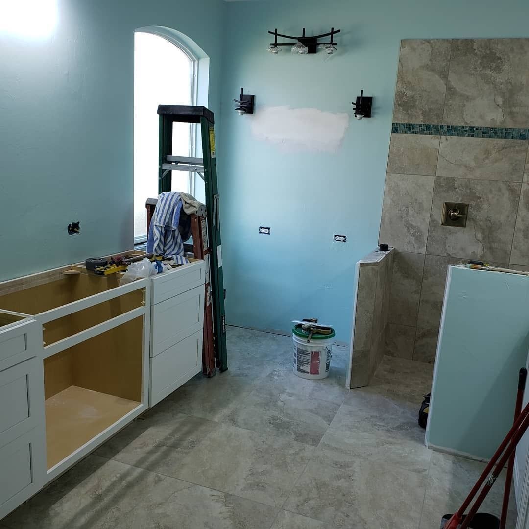 A bathroom under renovation with a new vanity cabinet, blue walls, a tile shower area, and tools on the floor.