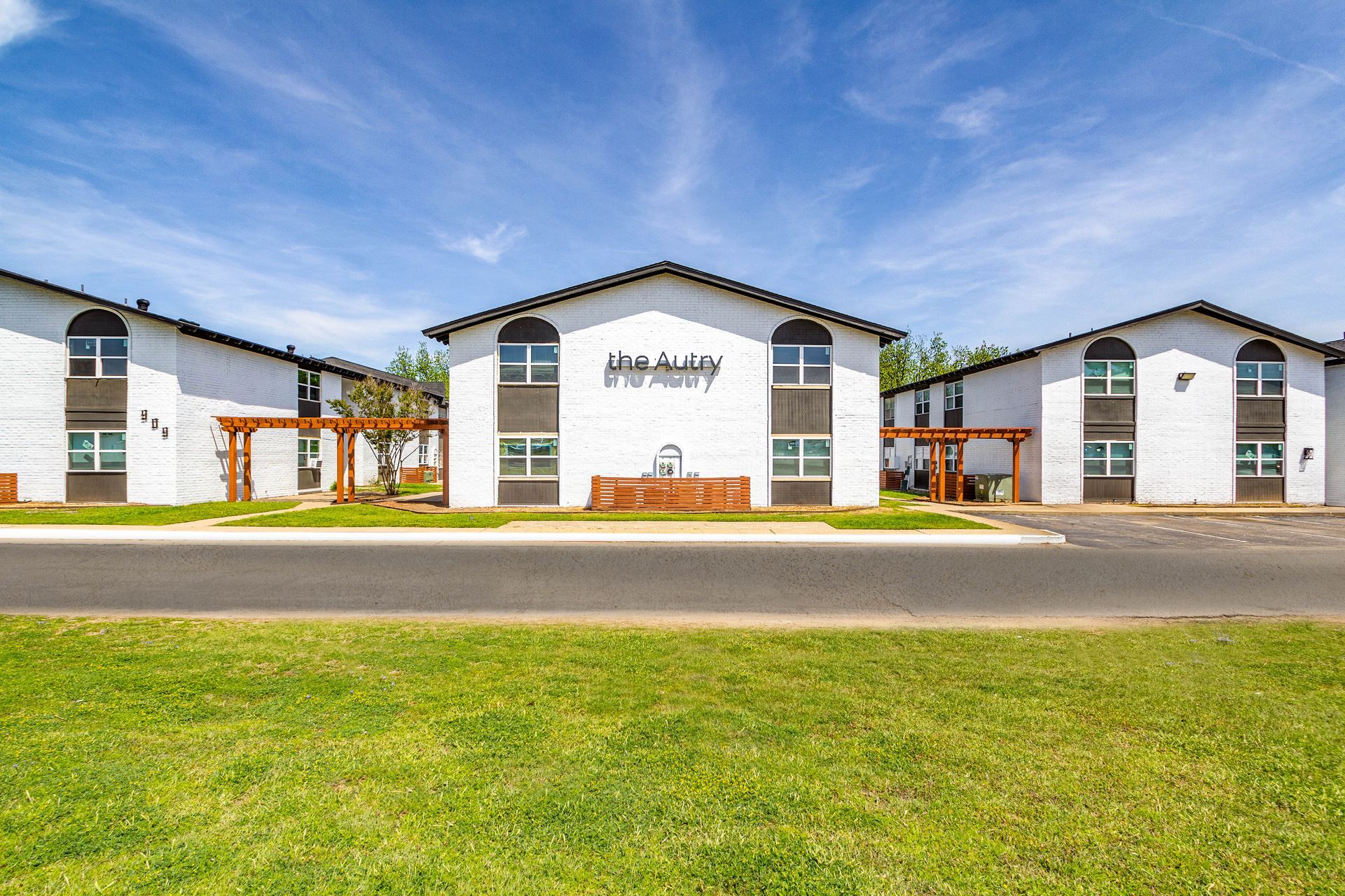 Apartment buildings with white walls, brown trim, and green lawn under a blue sky.