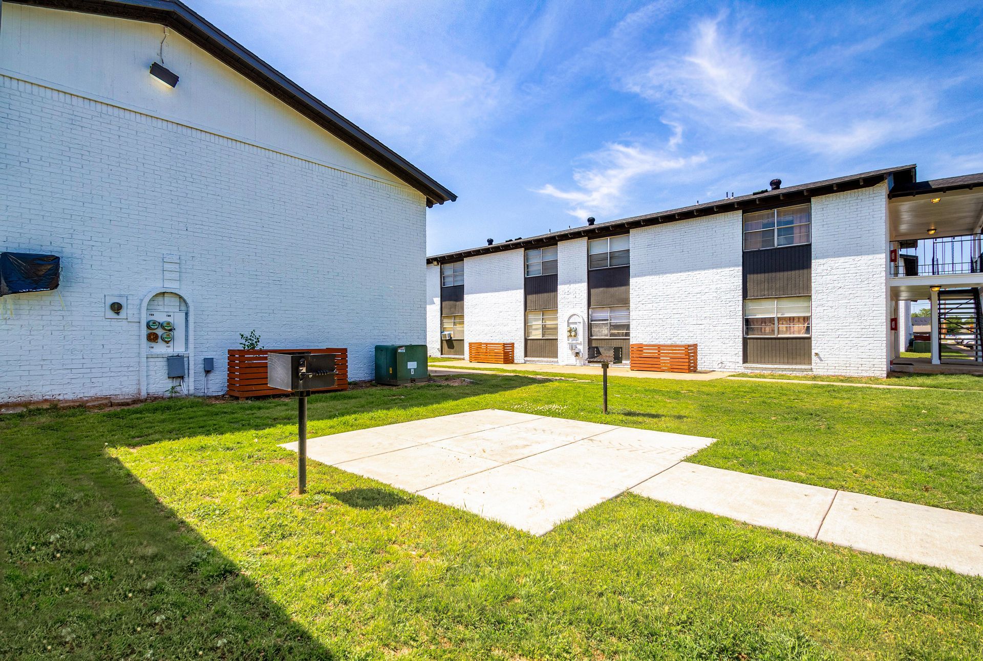 Apartment complex exterior with lawn, grilling area, and blue sky. White and black buildings.