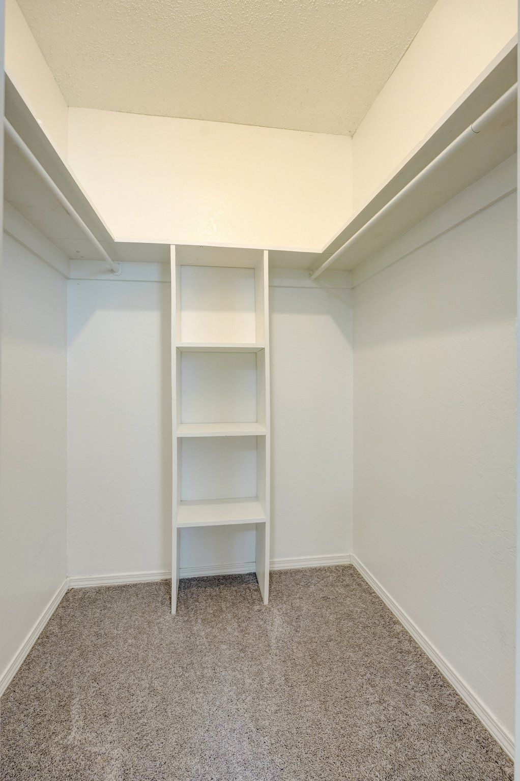 Empty white closet with shelves, a small set of shelves, and speckled carpet.