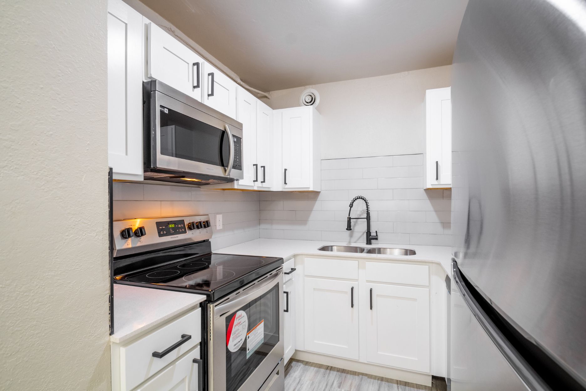White kitchen with stainless steel appliances, cabinets, and marble backsplash.