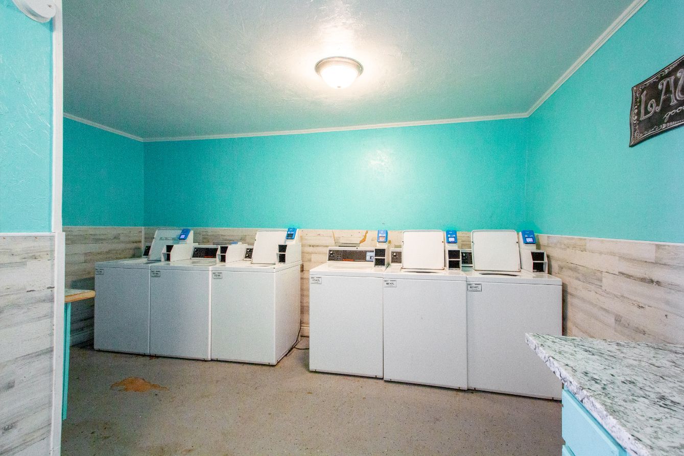 Laundry room with white washers and dryers, teal walls, and a speckled countertop.