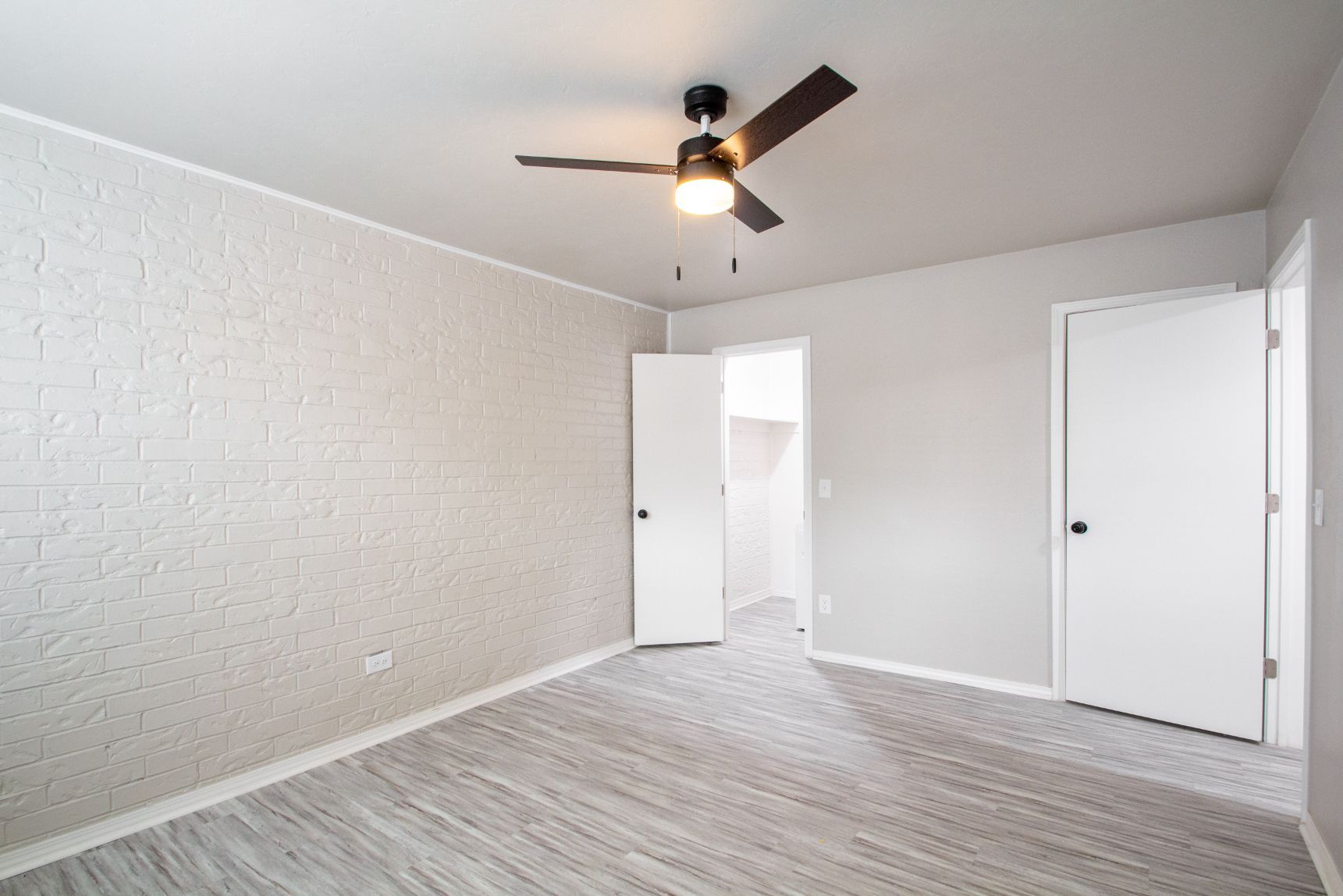 Bedroom with neutral-colored walls, a brick-like accent wall, gray carpet, ceiling fan, and open door to a closet.