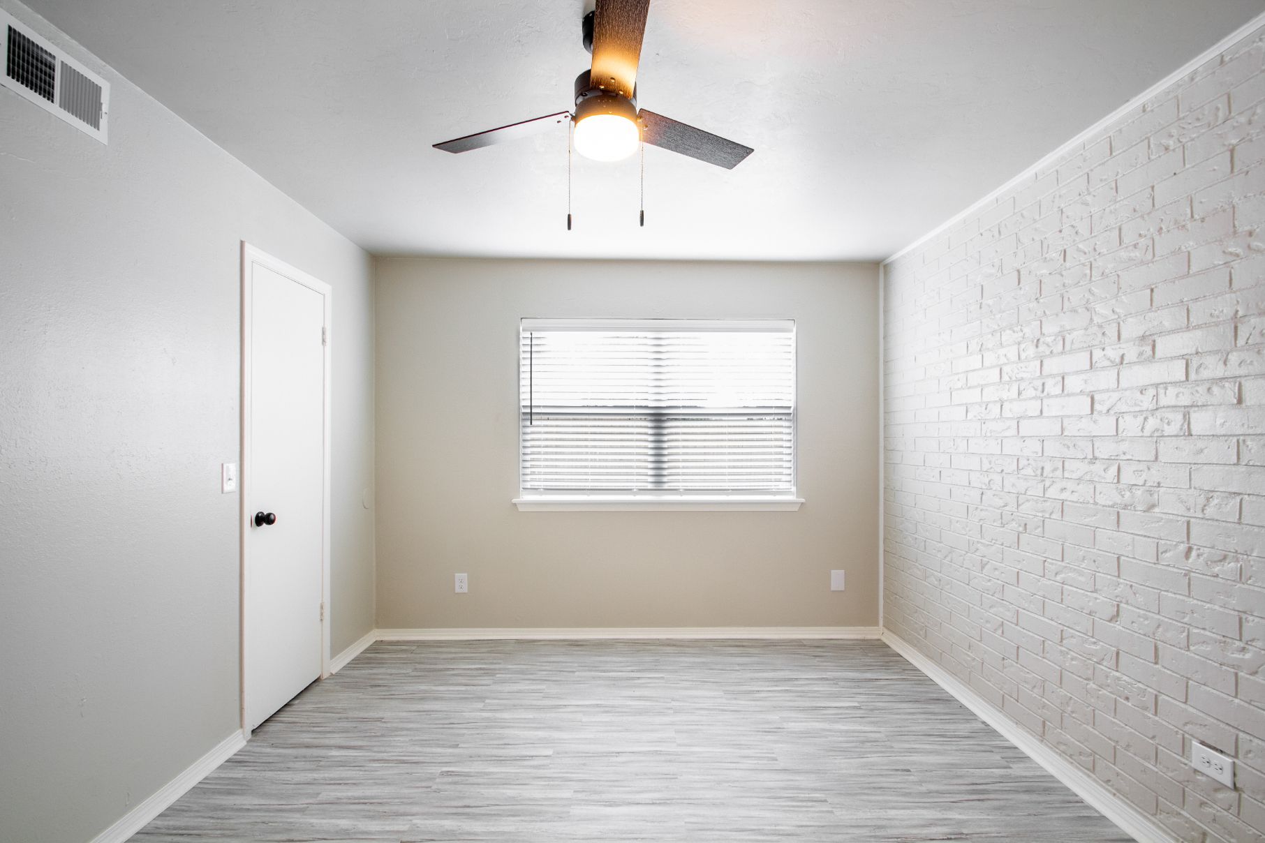 Empty room with grey walls, a ceiling fan, window, door, and brick wall.