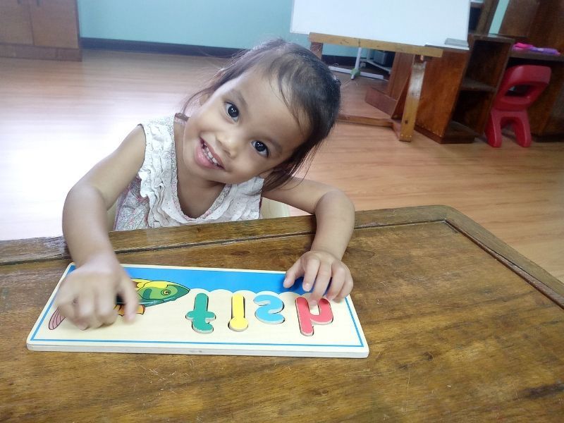 A little girl is smiling while playing with a puzzle