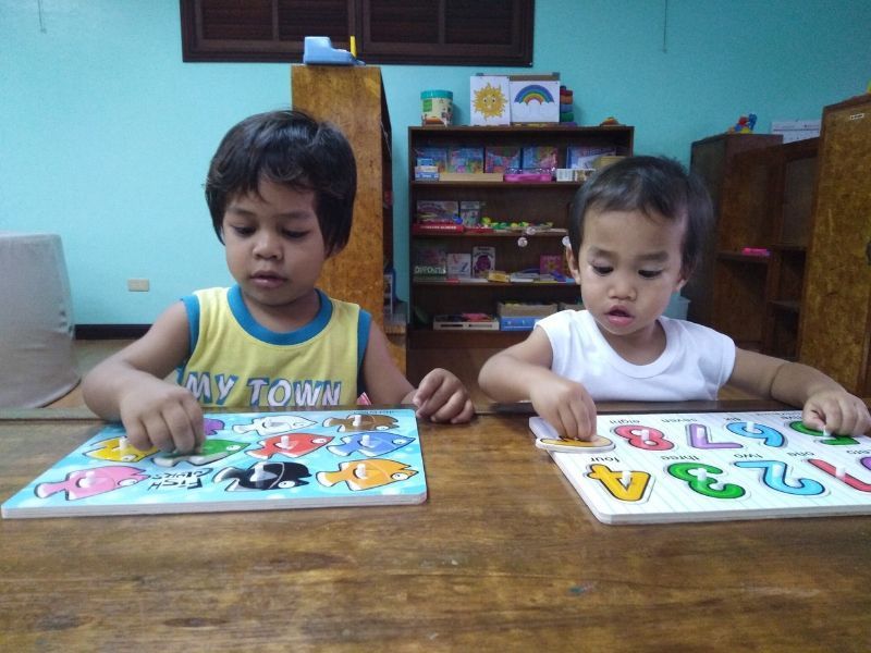 Two children are playing with puzzles and one of them is wearing a shirt that says my town