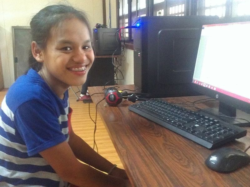 A young girl is smiling while sitting at a desk in front of a dell computer