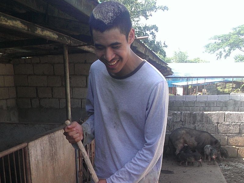 A man is smiling while holding a shovel in front of a pig pen