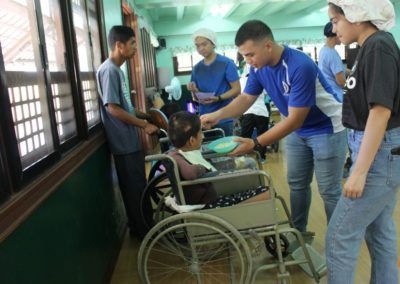 A man in a blue shirt is feeding a woman in a wheelchair.