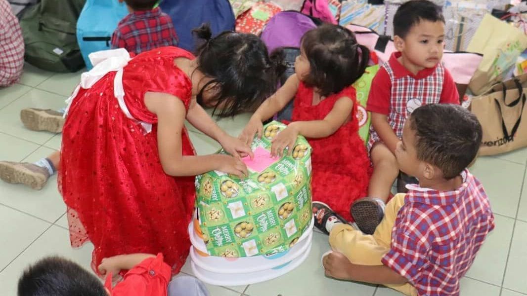 A group of children at the childrens foundation are sitting on the floor opening a present donated.