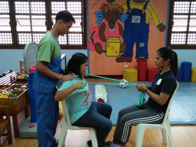 A woman is sitting in a chair while a man stretches her back