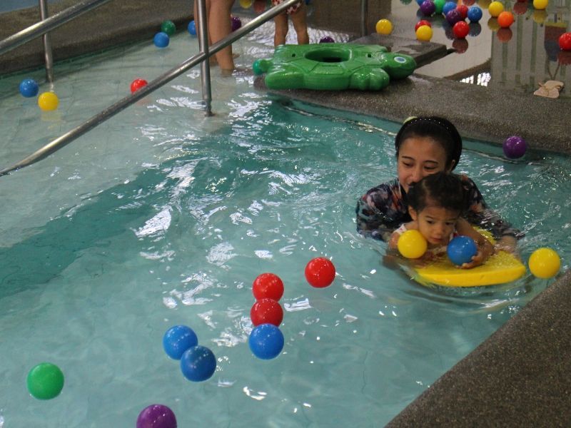 A woman and child are playing in a pool filled with colorful balls.