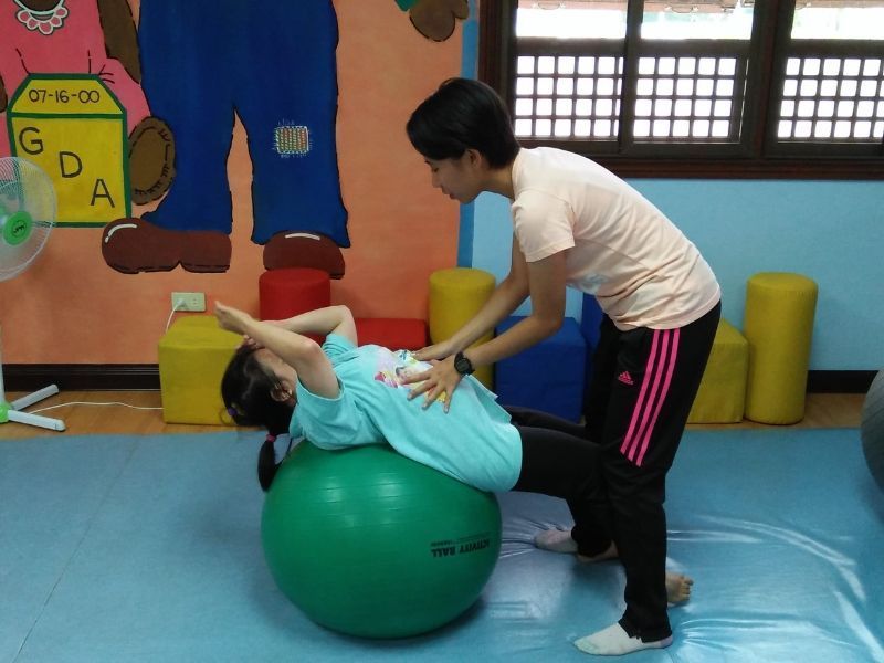A woman is helping a pregnant woman on a green exercise ball