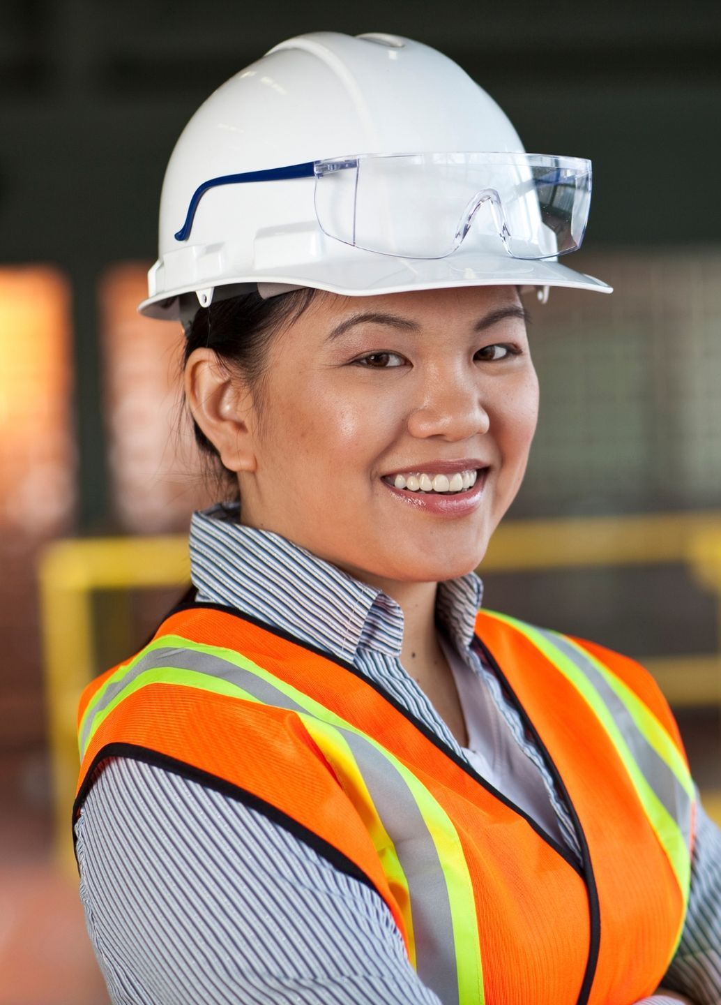 A woman wearing a hard hat and safety vest is smiling