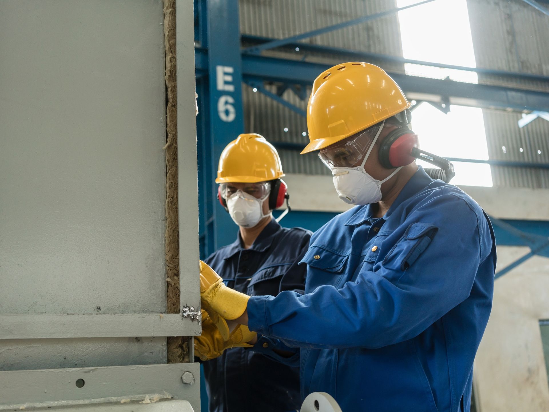 Two men wearing hard hats and masks are working in a factory.