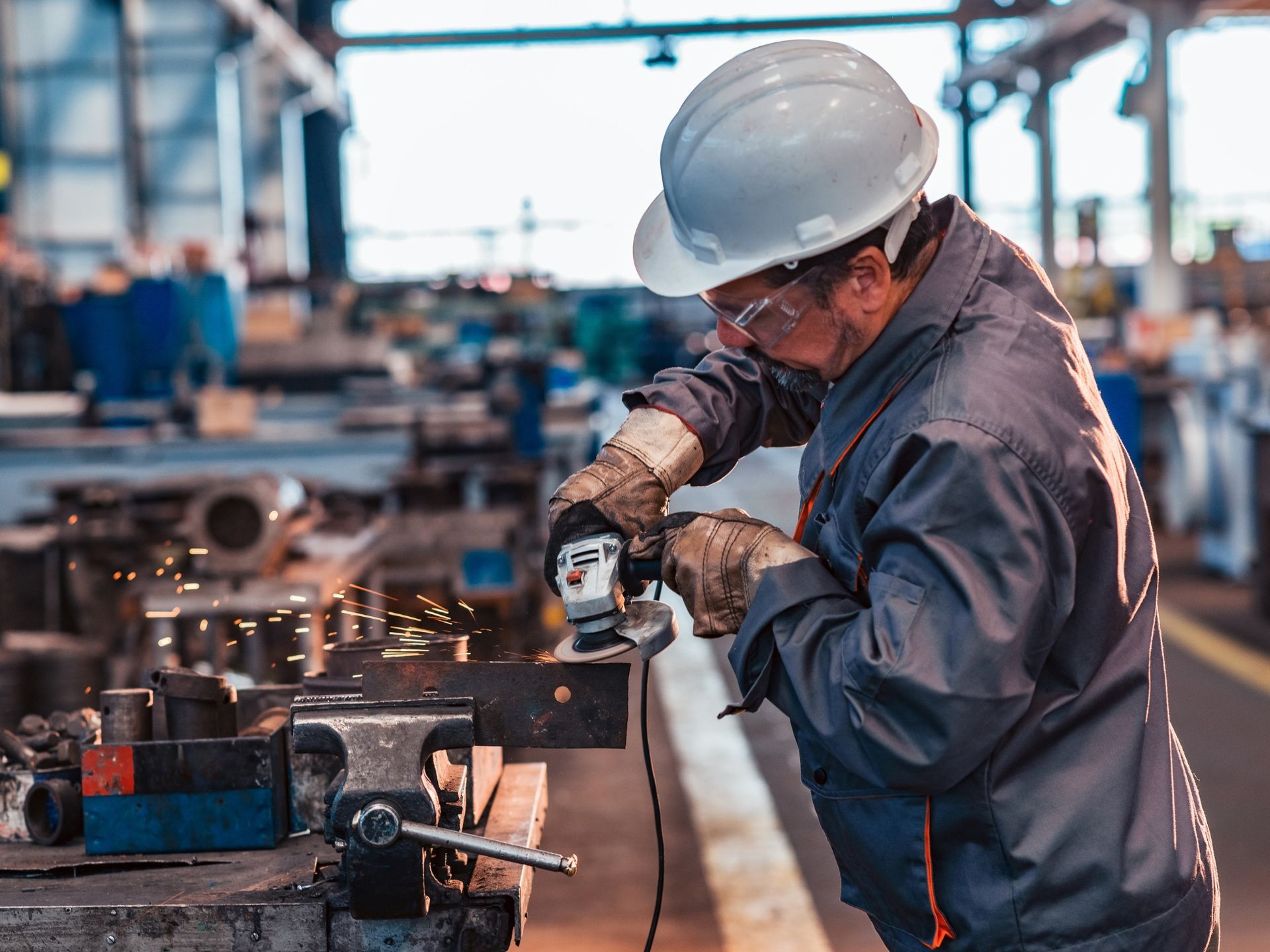 A man wearing a hard hat and safety glasses is working on a machine in a factory.