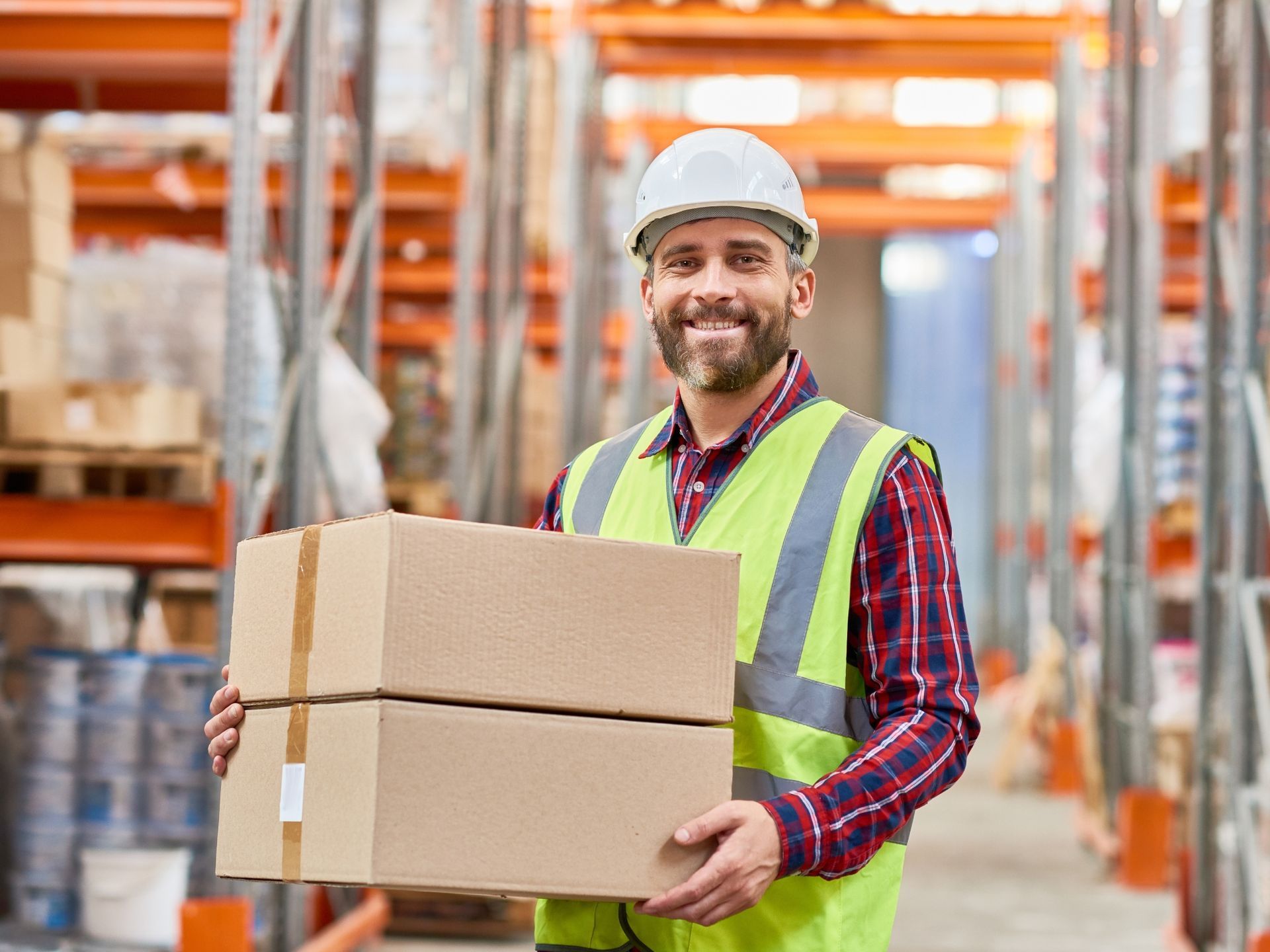 A man is holding a stack of cardboard boxes in a warehouse.