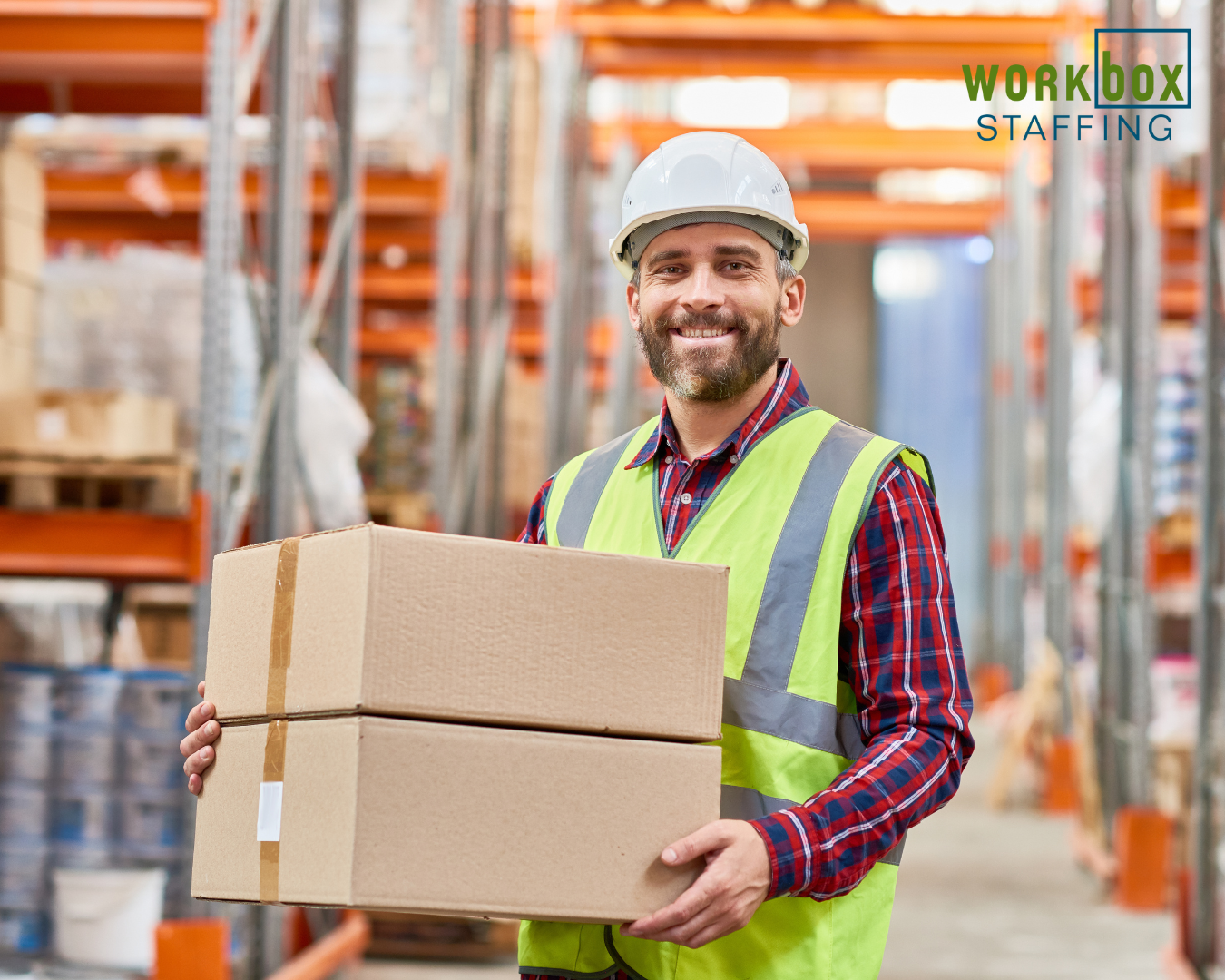 A worker is holding a box in a warehouse.