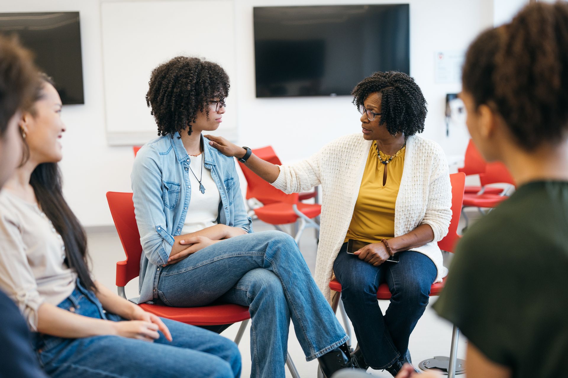 Woman in black top looks to the right, in meeting with others at table, tablet visible.