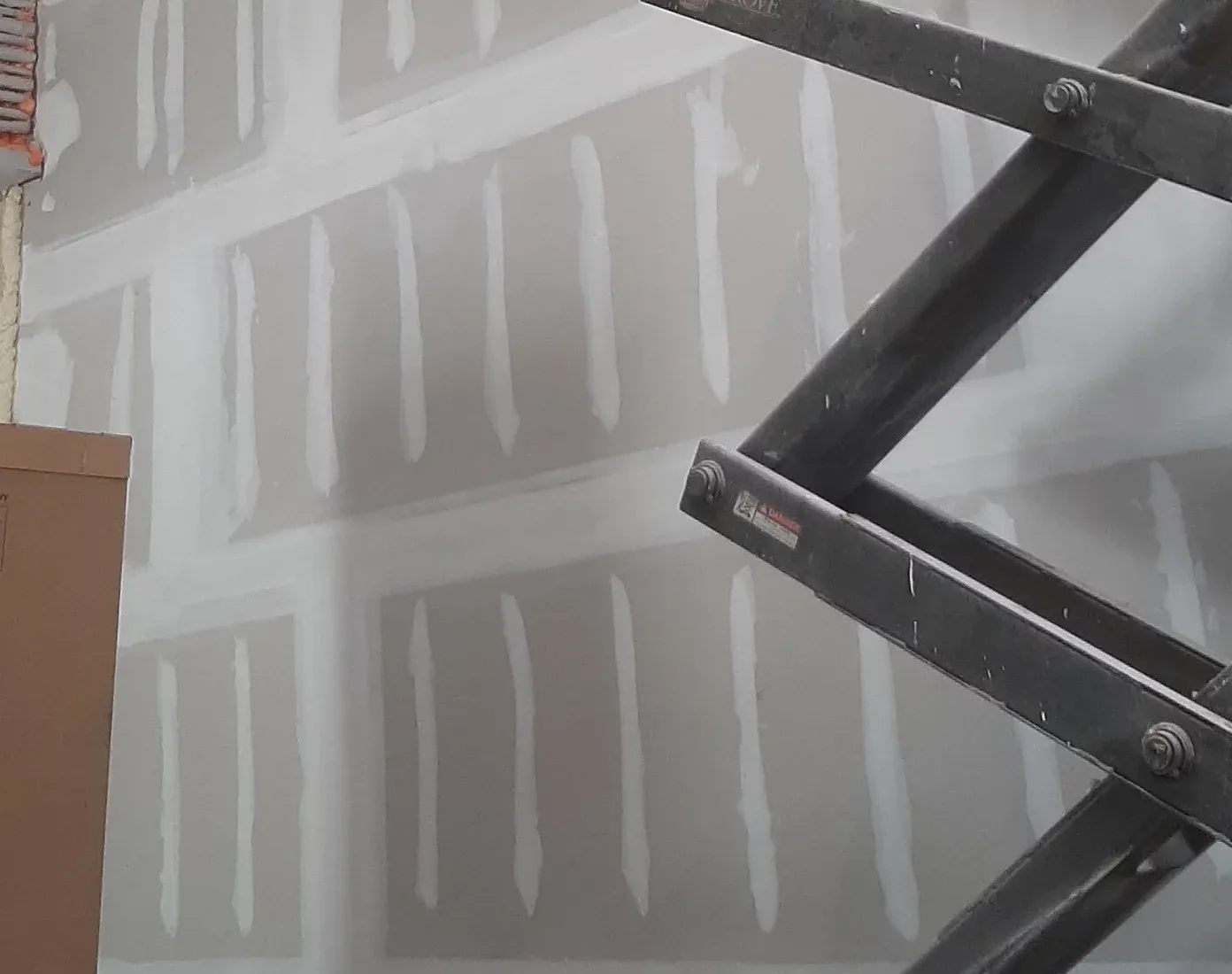 Drywall tools on a wooden surface: tape roll, sanding blocks, putty knives, and a taping knife.