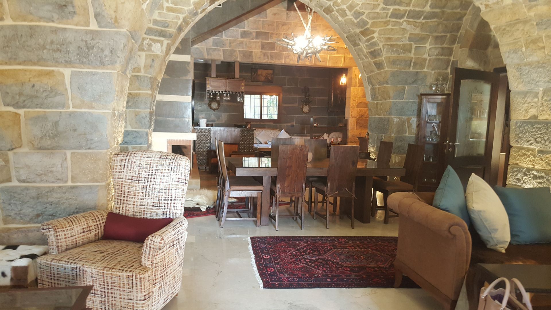 Stone archways frame a dining area with wooden table and chairs, rug, and a cozy armchair.
