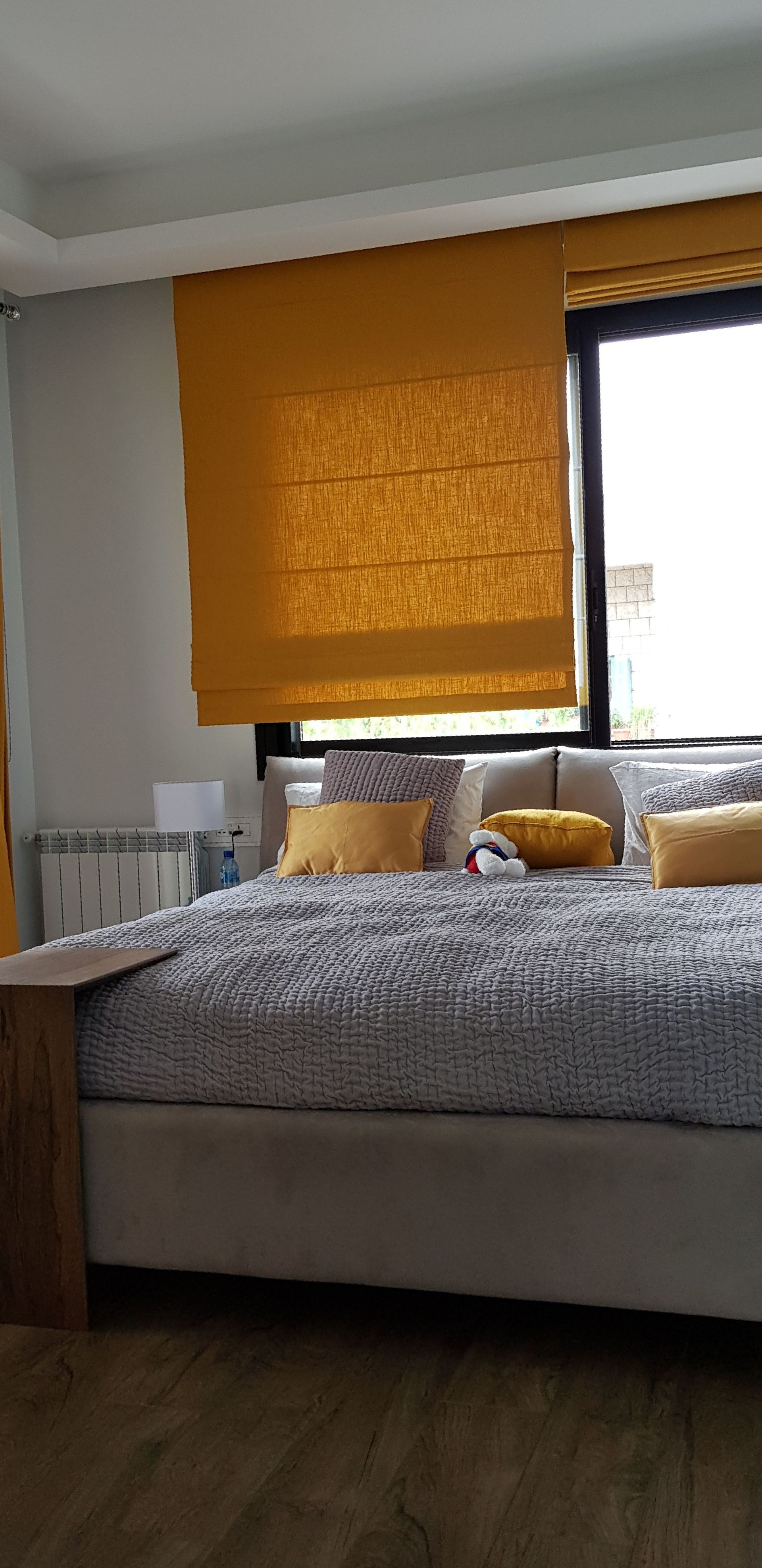 Bedroom with bed, mustard-yellow blinds, and a window overlooking the outside.