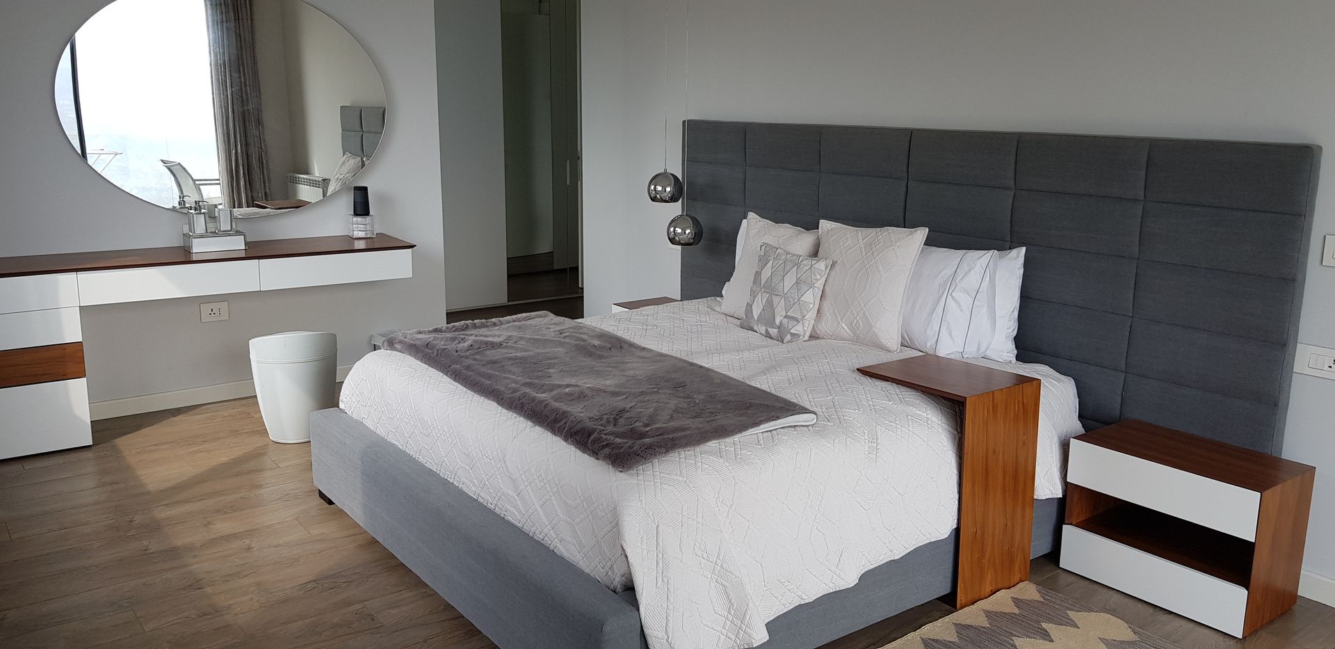 Modern bedroom with a gray bed, white bedding, and a vanity with a round mirror.