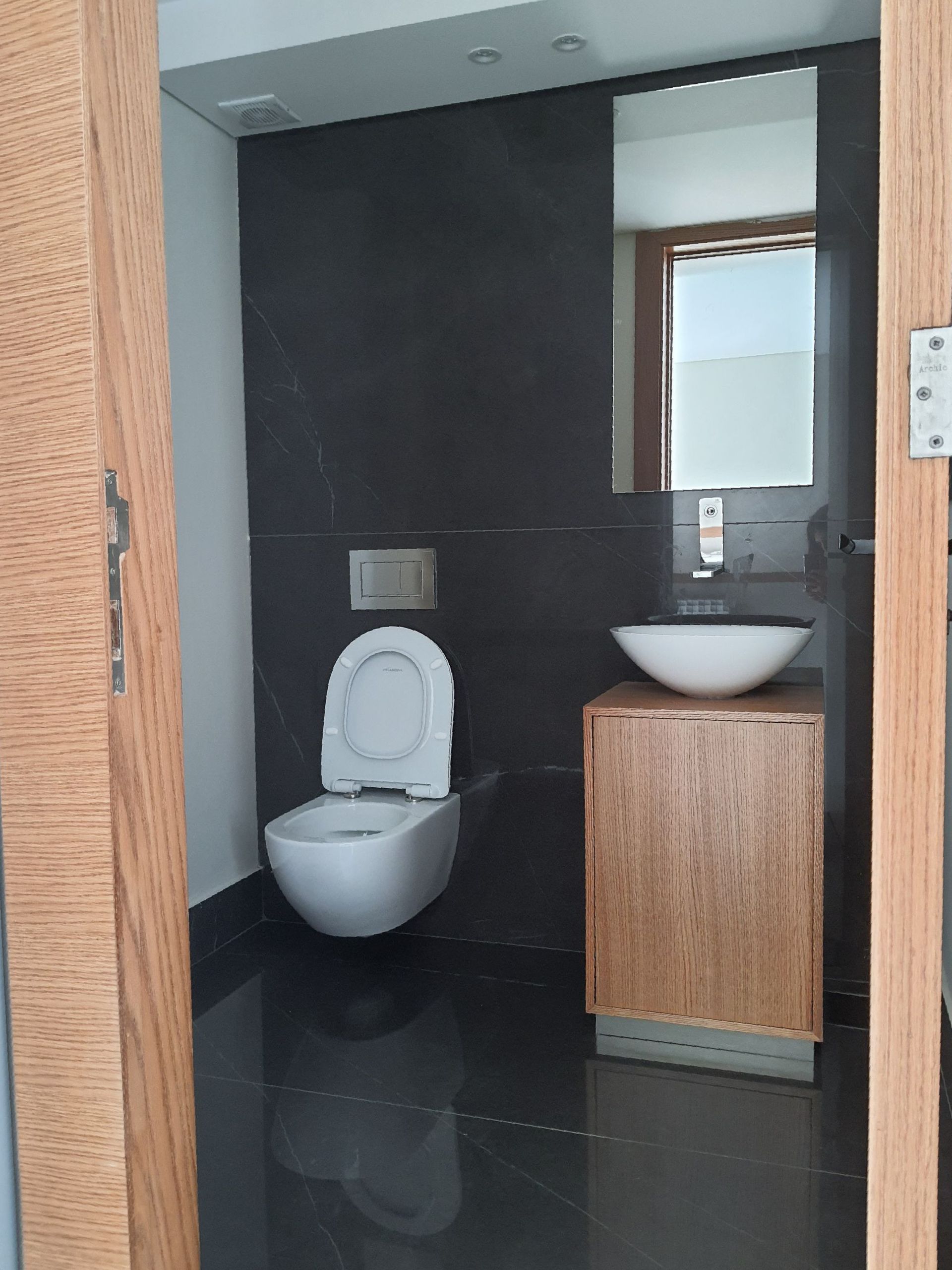 Modern bathroom with black walls, a white toilet, wooden cabinet and sink, and a large mirror.