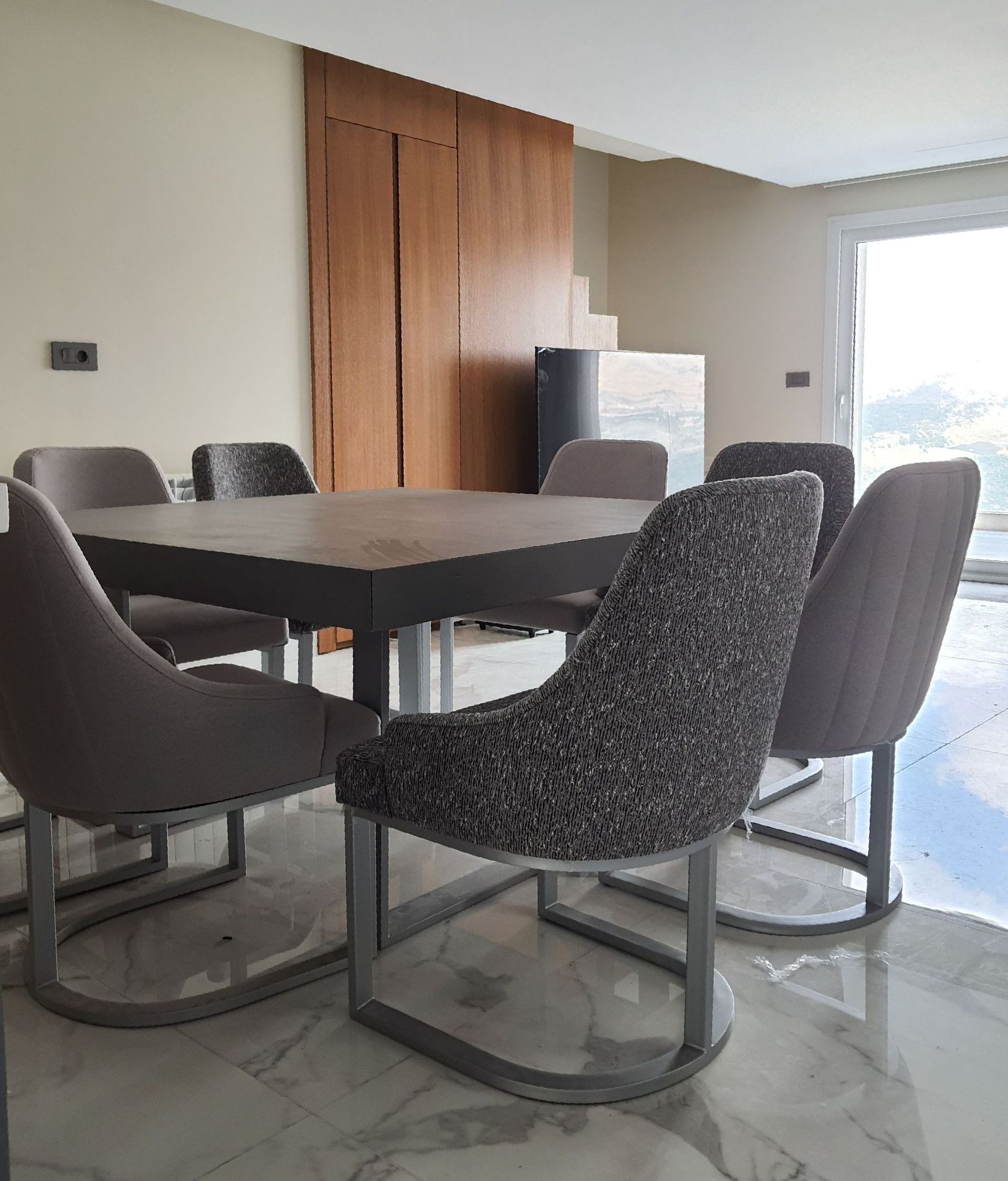 Dining room with square table and six chairs. One chair is textured. Neutral color scheme.